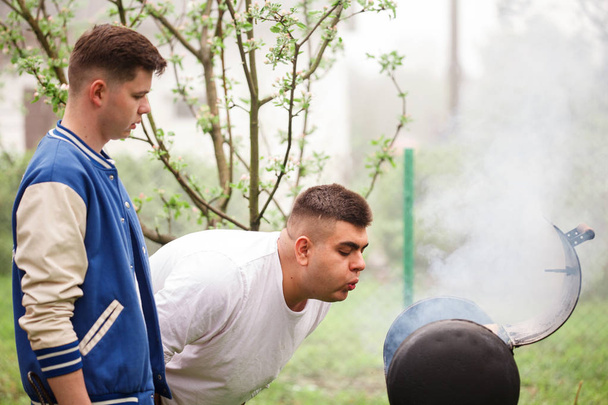 Barbekü ızgarası yanında duran iki genç adam. Açık havada ateş inanışı. - Fotoğraf, Görsel