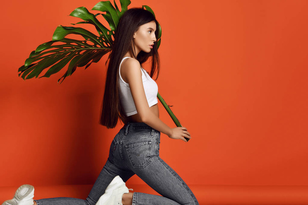 Young beautiful hipster girl in jeans and white top hold big tropical leaf - Foto, Imagem