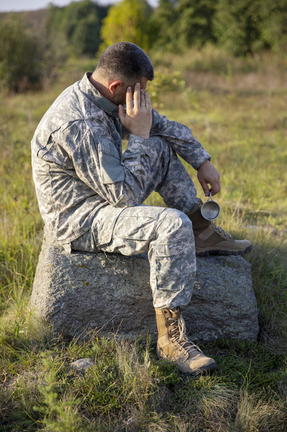 Ο στρατιώτης κάθεται και αναπαύεται. Λυπημένος και κουρασμένος στρατιώτης. Στρατιώτης - Φωτογραφία, εικόνα