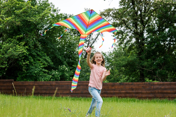 happy child running with colorful kite on green grass outside   - Photo, Image