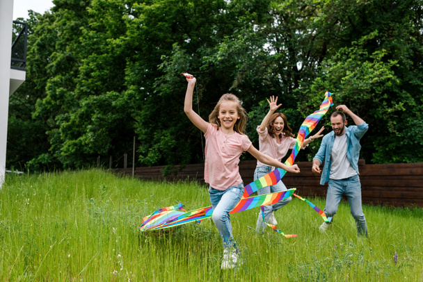 happy kid running with colorful kite near cheerful parents  - Photo, Image