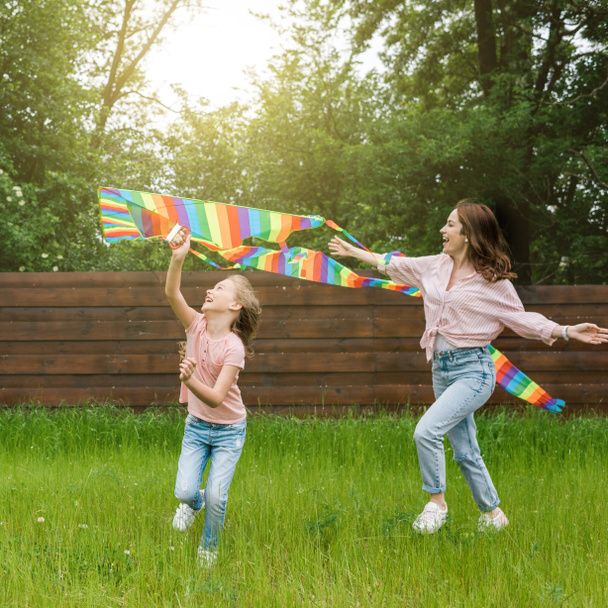 gelukkige moeder met uitgestrekte handen in de buurt van leuke jongen met kleurrijke vlieger  - Foto, afbeelding