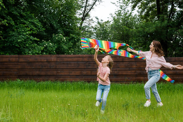 cheerful mother with outstretched hands near cute kid with colorful kite  - Foto, Imagen