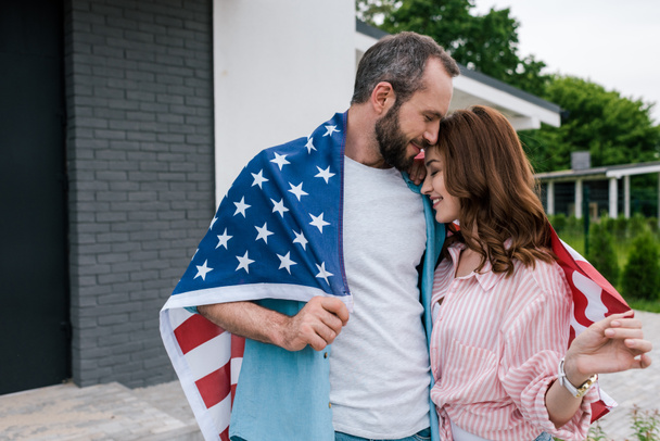 happy bearded man standing with cheerful woman and holding american flag  - Photo, Image