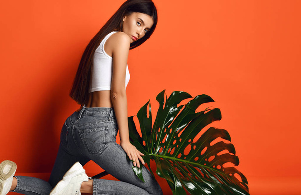 Young beautiful hipster girl in jeans and white top hold big tropical leaf - Foto, imagen