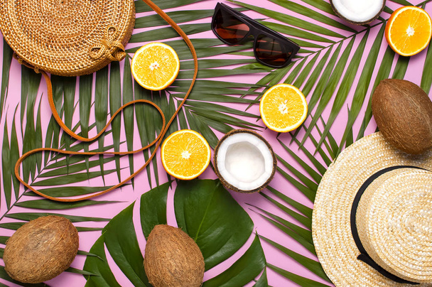 Summer fashion flat lay. Round trendy rattan bag straw hat sunglasses tropical palm leaves coconut orange on pink background. Top view copy space Trendy bamboo bag Creative background vacation concept - Photo, Image