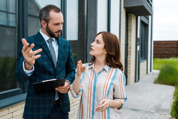 handsome bearded broker holding clipboard and gesturing near woman  - Photo, Image