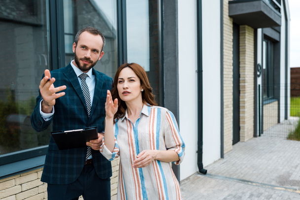 handsome broker holding clipboard and gesturing near attractive woman  - Photo, Image