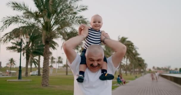 Yaşlı büyükbaba yaz aylarında boynunda oturan bir çocuk ile yürüyüş - Video, Çekim