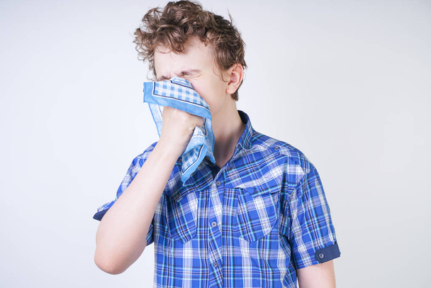 Allergiapoika, jolla on vuotava nenä nenäliinassa. Teini on ottaa huono terveys ja seisoo valkoinen studio tausta yksin
. - Valokuva, kuva