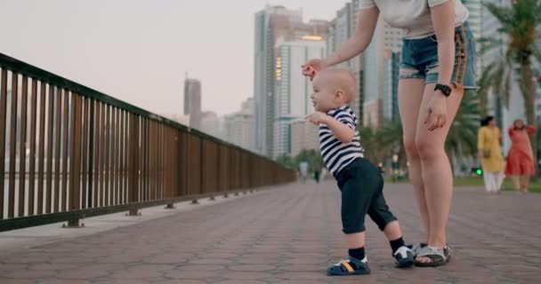 Usmívající se šťastné dítě bere první kroky v létě na nábřeží s mámou, ukazujícími prstem - Záběry, video