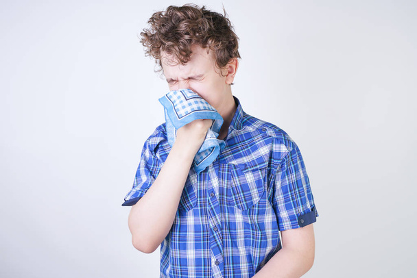 Allergie jongen kind met loopneus houden een zakdoek. Tiener heeft slechte gezondheid en staat op de witte studio achtergrond alleen. - Foto, afbeelding