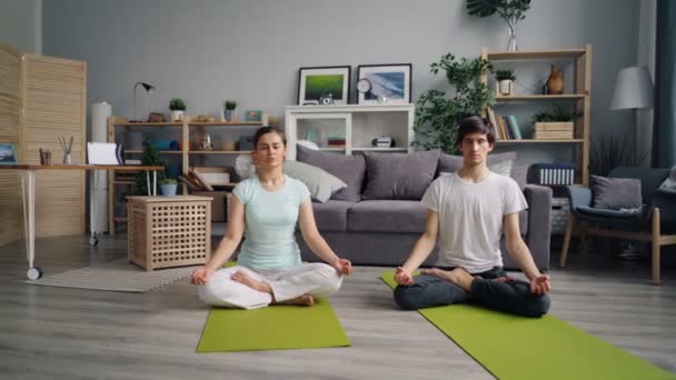 Menina e cara jovens meditando na posição de lótus no apartamento
 - Filmagem, Vídeo