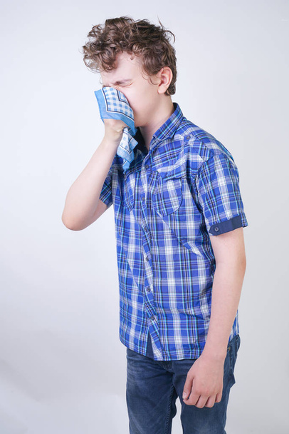 Алергія Хлопчик дитина з нежить тримає носову хустку. Підліток має погане здоров'я і стоїть на білому фоні студії
. - Фото, зображення