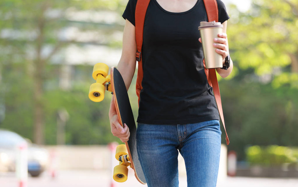 Woman walking with skateboard and cup of coffee on city street  - Foto, imagen