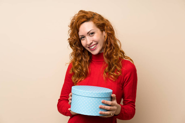 Redhead woman with turtleneck sweater holding gift box - Foto, afbeelding