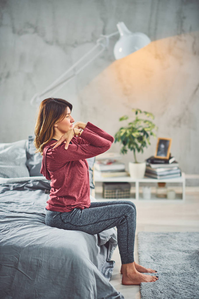 Okouzlující Kavkazská bruneta, která sedí na posteli v ložnici a provádí cvičení józ. - Fotografie, Obrázek