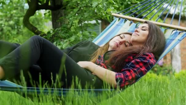 Lesbische paar liggen in hangmat in de tuin. Twee lesbiennes vriendinnen knuffel en slapen - Video