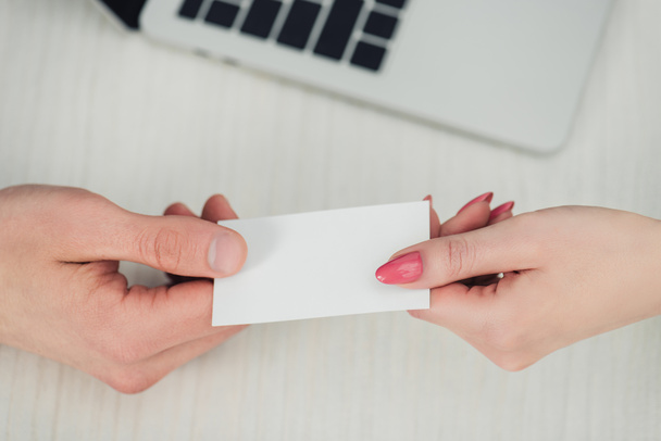 cropped view of male and female hands with white empty business card near laptop - Zdjęcie, obraz