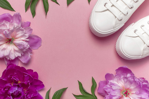 White female fashion sneakers and pink purple flowers peonies on pink background. Flat lay, top view, copy space. Women's shoes. Stylish white sneakers. Fashion blog or magazine concept. - Photo, image