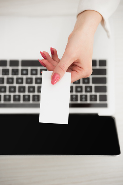 vista superior de la mujer de negocios sosteniendo blanco tarjeta de visita en blanco cerca del ordenador portátil
  - Foto, Imagen