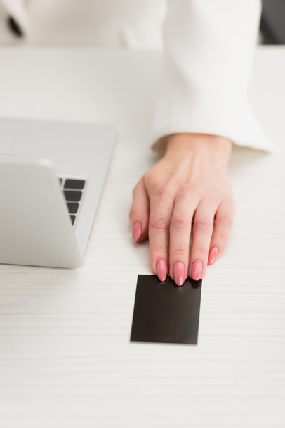partial view of businesswoman touching black empty business card while sitting at workplace - Φωτογραφία, εικόνα
