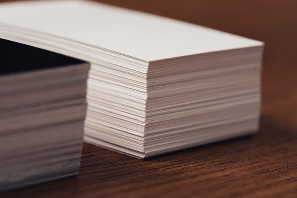 selective focus of stacked white and black empty business cards on brown wooden surface - Foto, afbeelding