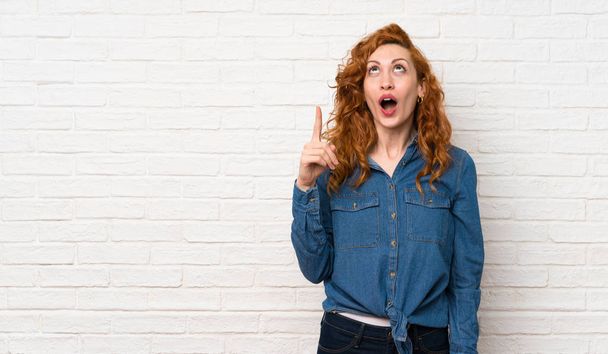 Redhead woman over white brick wall pointing up and surprised - Photo, Image