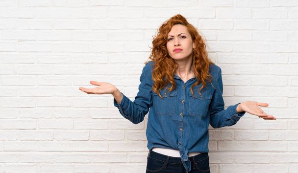 Redhead woman over white brick wall unhappy for not understand something - Φωτογραφία, εικόνα