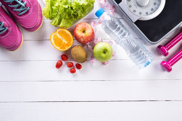 Healthy lifestyle, food and sport concept. Top view of athlete's equipment Weight Scale measuring tape blue dumbbell, sport water bottles, fruit and vegetables on white wooden background. - Photo, Image