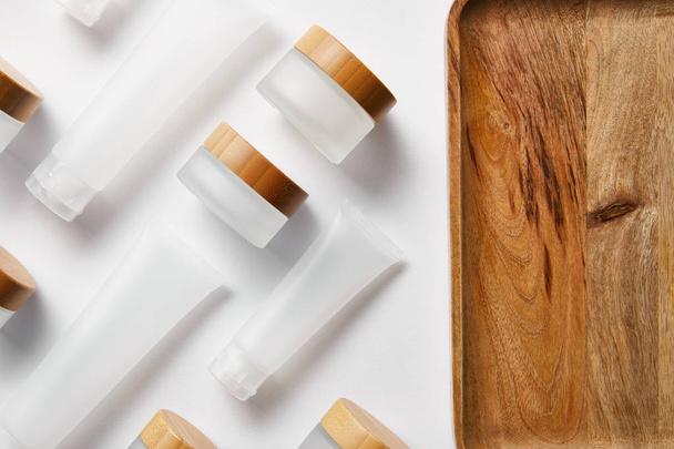 flat lay of cream tubes and jars near wooden tray on white  - Photo, Image