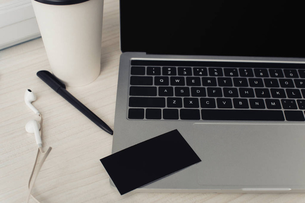 black empty business card on laptop keyboard, pen and earphones on office table - Foto, afbeelding