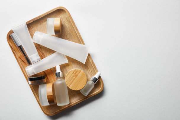 abundância de recipientes cosméticos vazios na bandeja de madeira no branco
  - Foto, Imagem