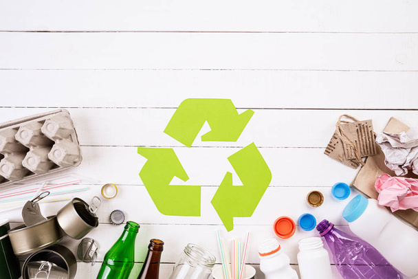 Vista superior de diferentes materiais de lixo com símbolo de reciclagem no fundo da mesa de madeira branca. Reciclagem, Dia Mundial do Meio Ambiente e Conceito Eco
 - Foto, Imagem