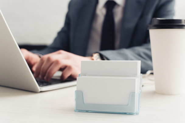 partial view of businessman using laptop near card holder with empty business cards - Photo, Image