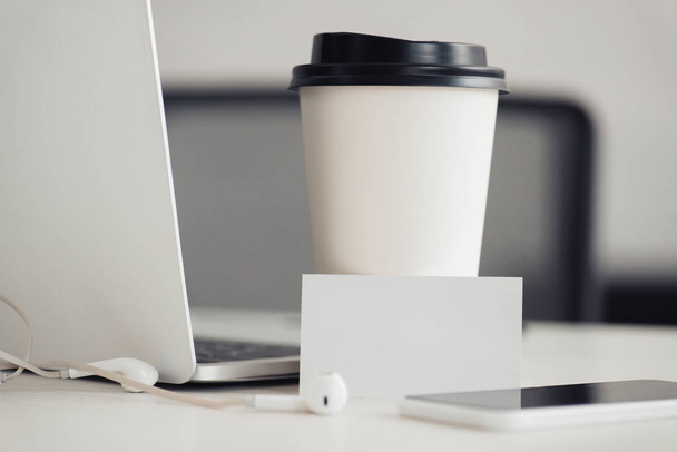 üres névjegykártyák közelében eldobható csésze, laptop és okostelefon az irodai asztal - Fotó, kép