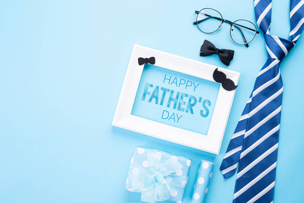 Happy fathers day concept. Top view of blue tie, beautiful gift box, white picture frame with Happy father's day text on bright blue pastel background. Flat lay. - Photo, Image