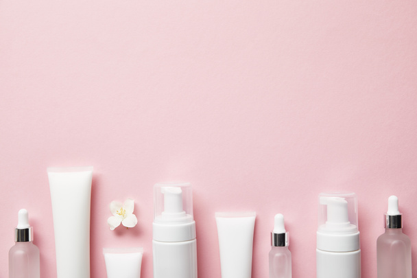vista superior de botellas de vidrio cosmético, tubos de crema con crema, dispensadores de cosméticos y flor de jazmín en rosa
  - Foto, imagen
