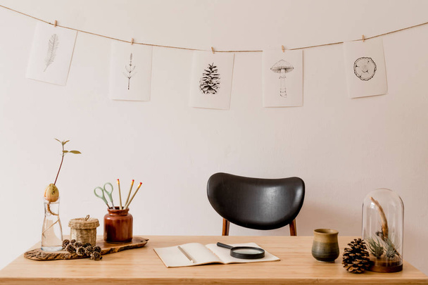 Scandinavian interior of home office space with wooden desk, design chair, forest accessories, avocado plant, office supplies. Stylish drawings on the white wall. Botanical home decor. Minimalistic. - Φωτογραφία, εικόνα
