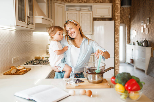 Young mother and her daughter prepares pastry with melted chocolate. Cute woman and little girl cooking on the kitchen. Happy family makes sweet dessert at the counter - Photo, Image