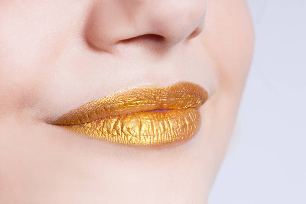 Beautiful closeup female lips with gold color makeup - 写真・画像