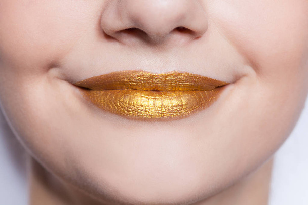 Beautiful closeup female lips with gold color makeup - 写真・画像