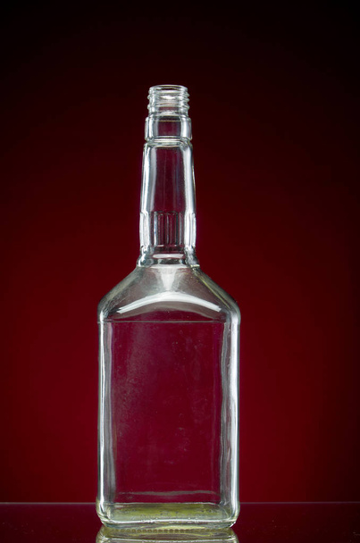 Transparent empty alcohol bottle on red background - Foto, afbeelding