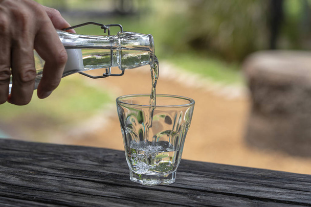 ein Kellner in einem Restaurant schüttet frisches Wasser aus einer Flasche in ein Glas, Nahaufnahme - Foto, Bild