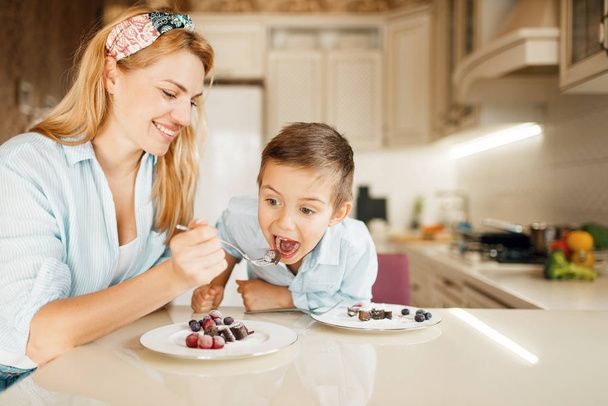 Mladá matka s dítětem ochutnává čokoládové těsto. Roztomilá žena a malý chlapec vaří v kuchyni. Happy rodina ochutnávka sladký dezert u pultu a baví - Fotografie, Obrázek