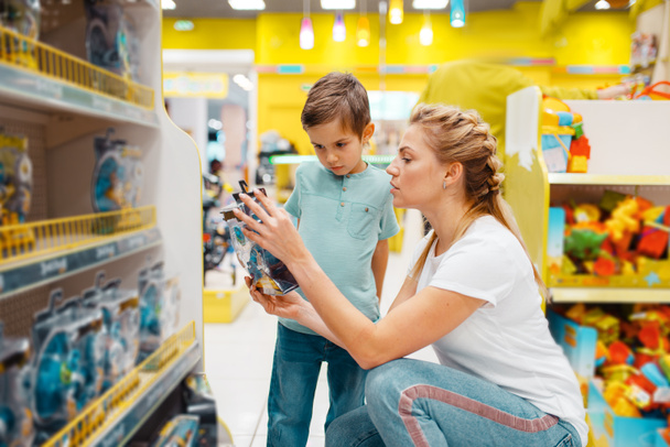 Happy mother with her little son choosing toys in kids store. Mom and child have a purchase in supermarket together, family shopping - Foto, Imagen
