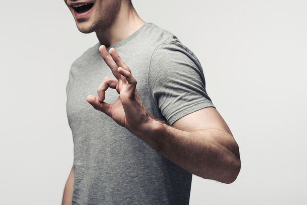bijgesneden weergave van de jonge man met OK gebaar geïsoleerd op grijs, menselijke emotie en expressie concept - Foto, afbeelding