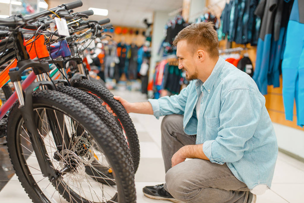 Man checks bicycle tyre, shopping in sports shop. Summer season extreme lifestyle, active leisure store, customer buying cycle equipment - Photo, Image
