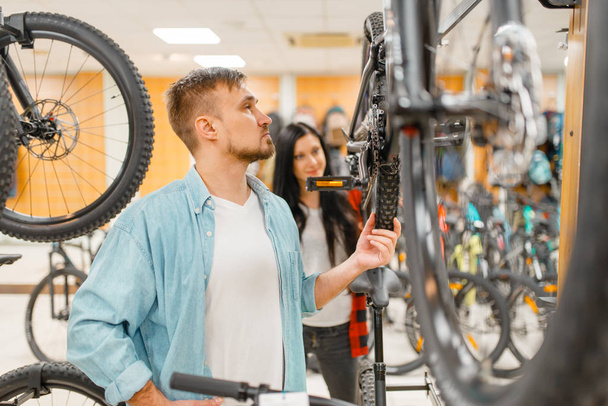 Man checks bicycle disk breaks, shopping in sports shop. Summer season extreme lifestyle, active leisure store, customers buying cycle, couple choosing bikes - Photo, Image