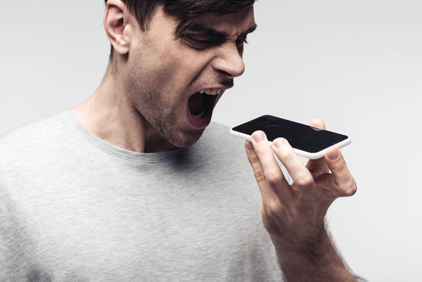 angry man quarreling on smartphone isolated on grey - 写真・画像